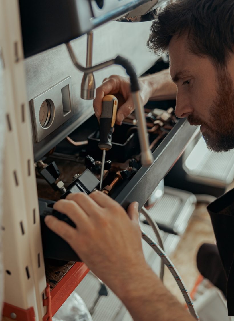 Handsome worker in uniform repairing coffee machine in a workshop